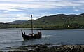 Un bateau viking flotte près d’un rivage rocheux, rappelant les voyages historiques des drakkars.