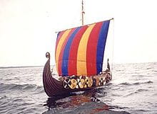 Un bateau viking avec une voile rouge et bleue sur la mer dans l’article ’The Longships’.