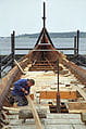 Homme réparant un bateau sur l’eau, incarnant l’esprit des anciens drakkars vikings.